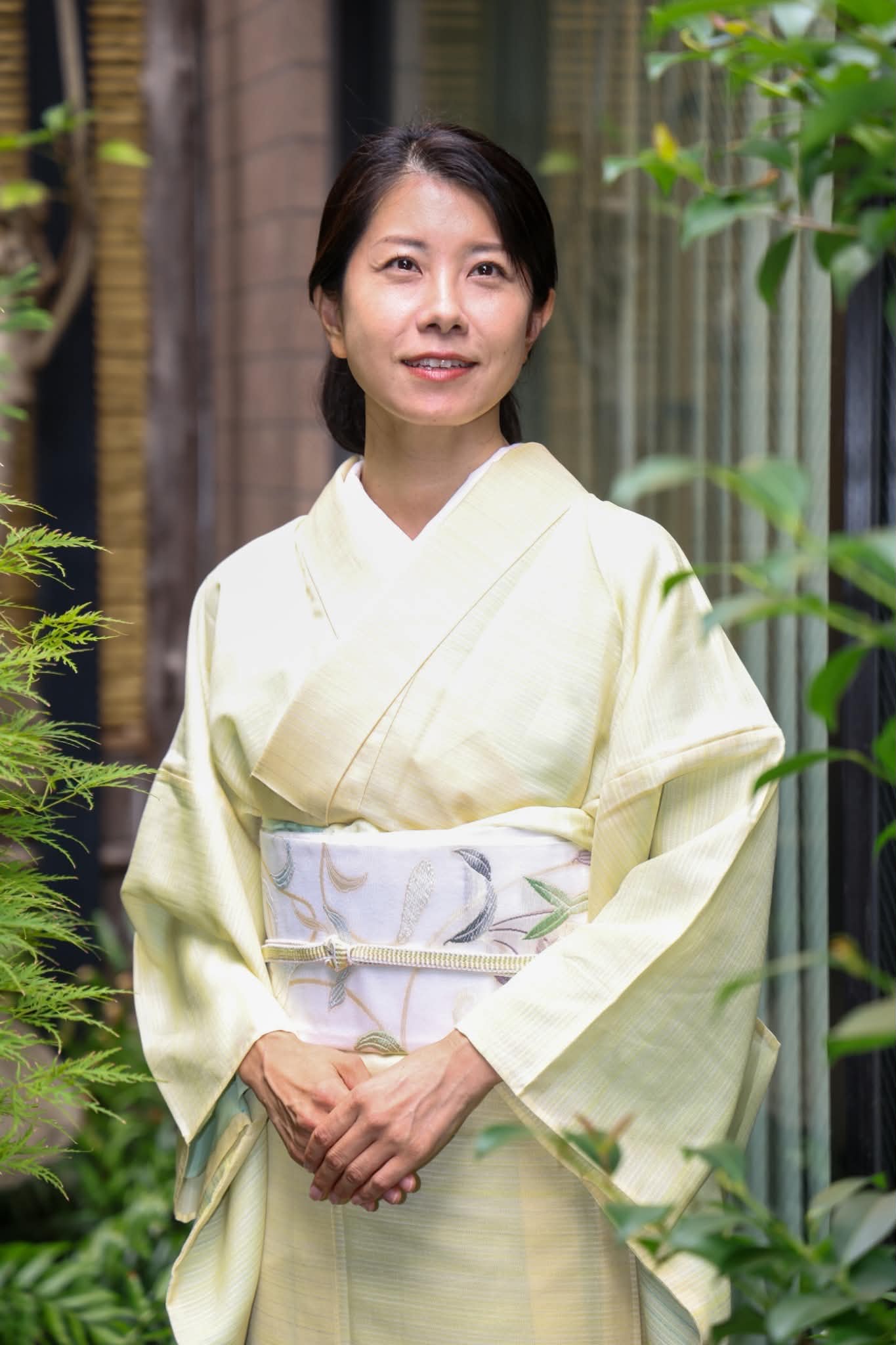 淡い黄色の着物を着て庭に立つ田原香織さん